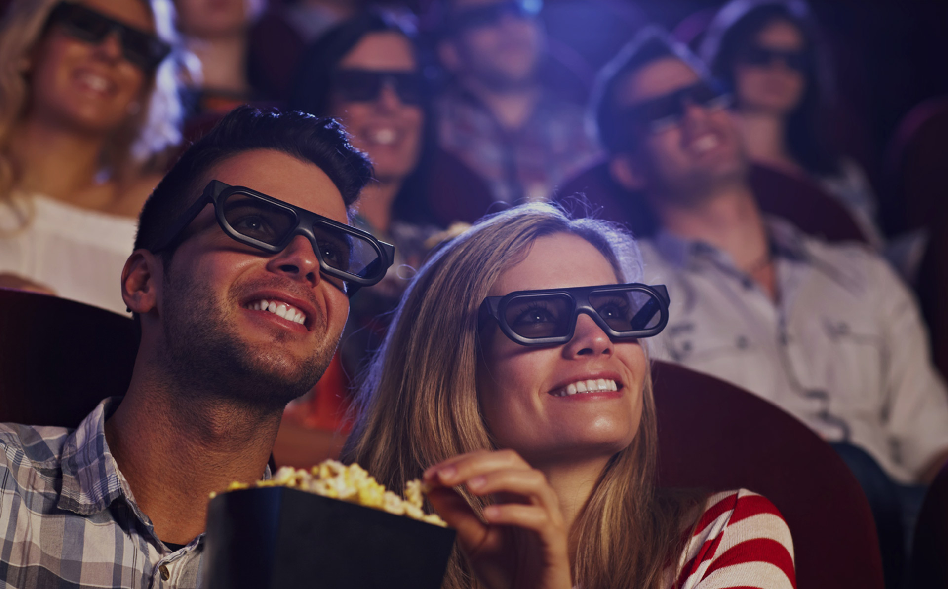 A man and woman at the cinema with 3D glasses enjoying popcorn.