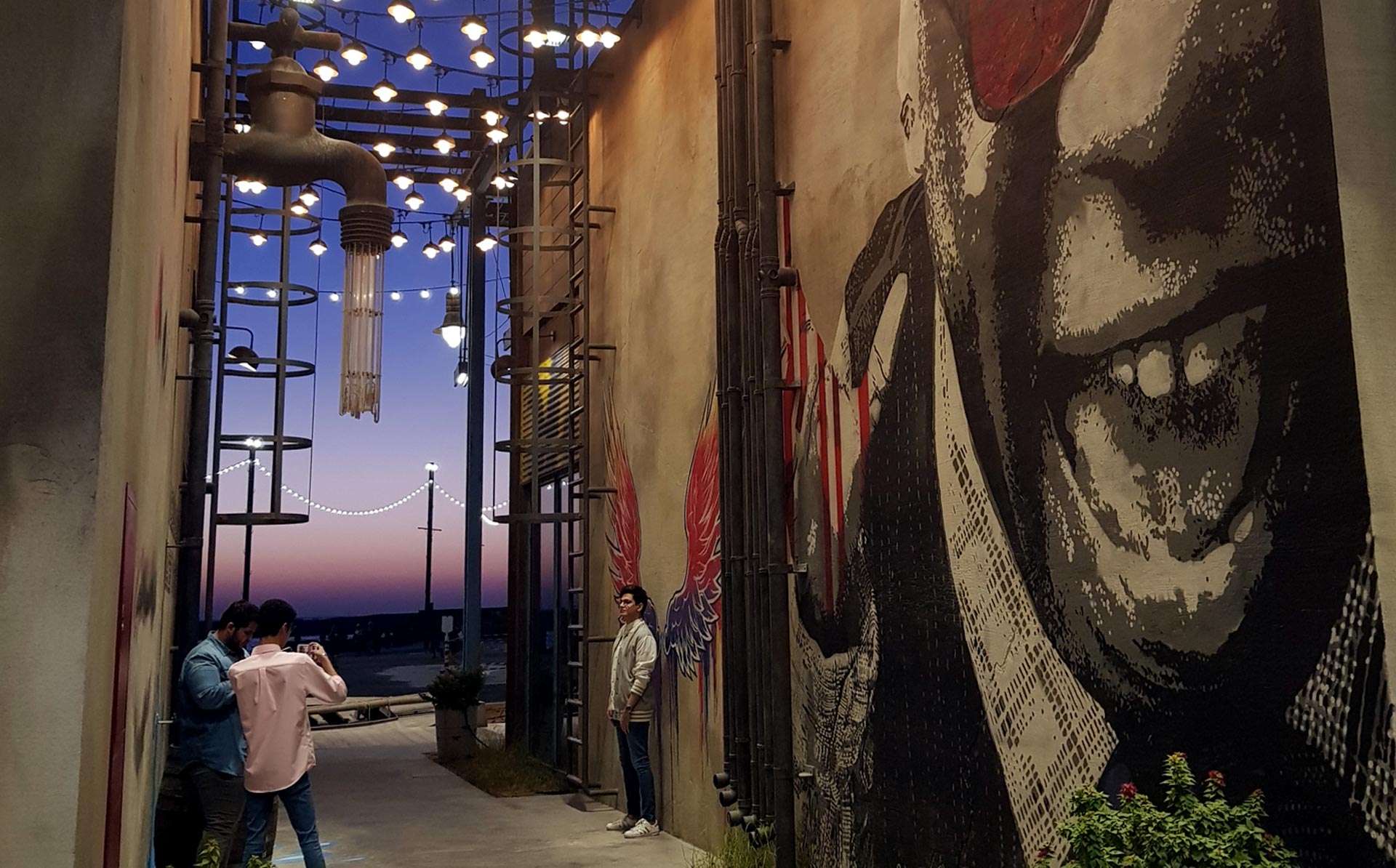 People taking photos at La Mer, Dubai at sunset with graffiti art on the wall.